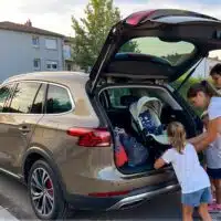 Famille chargeant le coffre spacieux d’une voiture familiale stationnée en zone résidentielle, avec sièges enfants et bagages, illustrant les besoins d’espace, de modularité et de praticité d’un véhicule adapté à la vie familiale.