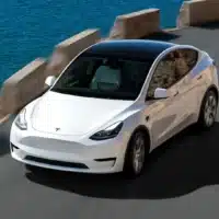 SUV électrique Tesla blanc roulant sur une route côtière, avec la mer et des falaises en arrière-plan, illustrant la fiabilité et la mobilité électrique moderne.