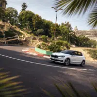Skoda Fabia 130 blanche engagée dans un virage serré sur route urbaine sinueuse, illustrant le dynamisme et le plaisir de conduite d’une citadine sportive thermique, dans un environnement méditerranéen.
