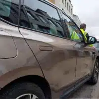 Poignées affleurantes sur une voiture électrique moderne stationnée en ville, avec un intervenant à proximité de la portière.