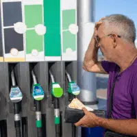 Automobiliste regardant les pompes d’une station-service en tenant son portefeuille face à la hausse du prix des carburants.