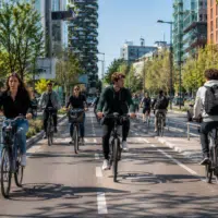 Groupe d’adolescents et de jeunes adultes circulant à vélo sur une piste cyclable sécurisée dans une ville européenne moderne avec vélos classiques et électriques.