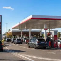 Station-service moderne en France pendant un week-end chargé avec plusieurs voitures faisant le plein et affichage de prix du carburant élevés.